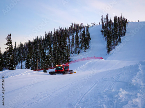 Red snow groomers clean the slope of the mountain in the mountain ski resort of Gornaya Salanga. Special machinery works on a winter evening © Евгений Казанцев