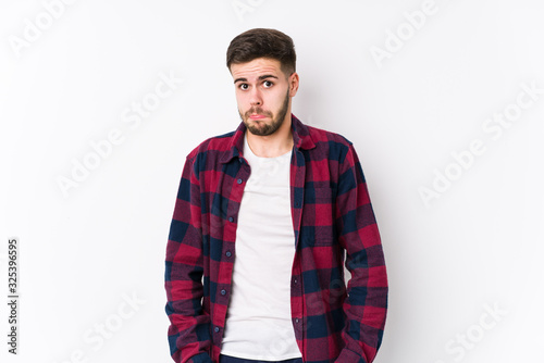 Young caucasian man posing in a white background isolated shrugs shoulders and open eyes confused.