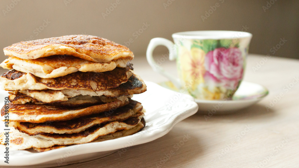 Low Carb Keto Diet Pancakes from almond coconut flour stack on white plate and cup of cocoa on wooden table background close up view. Selective focus. Copy space. Ketogenic concept Low Carb Keto Diet Pancakes from almond coconut flour stack on white plate and cup of cocoa on wooden table background close up view. Selective focus. Copy space. Ketogenic concept