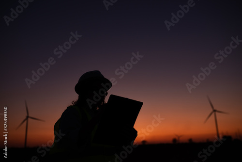 Silhouette of women engineer working and holding the report at wind turbine farm Power Generator Station on mountain,Thailand people