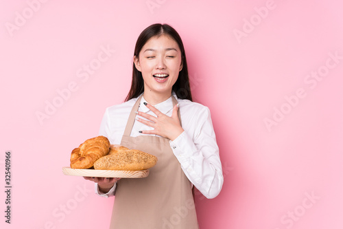Young chinese baker woman isolated laughs out loudly keeping hand on chest.