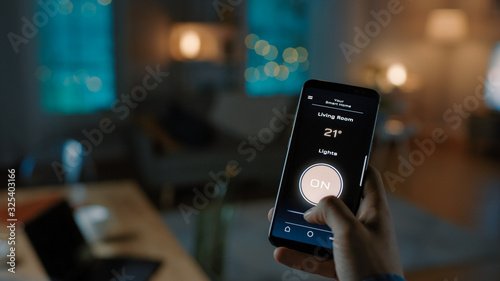 Close Up Shot of a Smartphone with Active Smart Home Application. Person is Tapping the Screen To Turn Lights On/Off in the Room. It's Cozy Evening in the Apartment. 