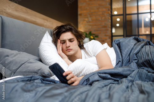 Sleepy male waking up early after hearing alarm clock signal on monday morning