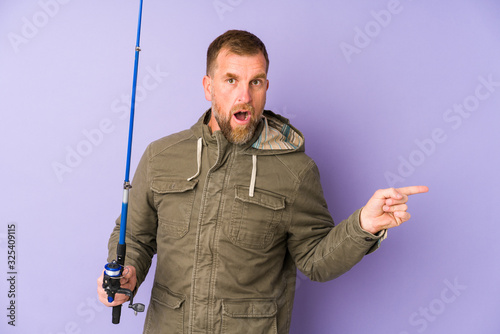 Senior fisherman isolated on purple background pointing to the side