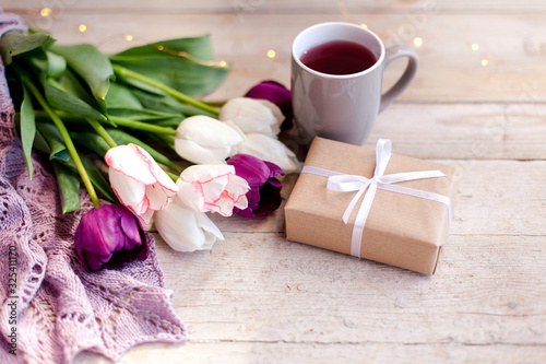 Spring flowers. Tulips  gift box and white cup of tea at wooden background. White  pink  lilac and purple bouquet. Morning surprise. Still life.