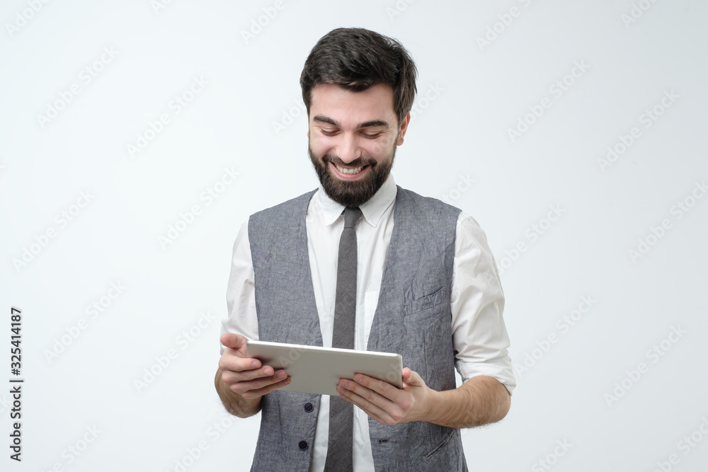 Attractive hispanic man with touchpad smiling reading news on tablet Attractive hispanic man with touchpad smiling reading news on tablet