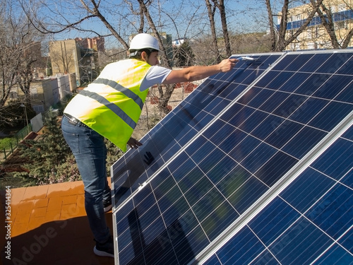 Caucasian attractive young technician looking at the solar panels with a glass cleaner wiper in his hand photo