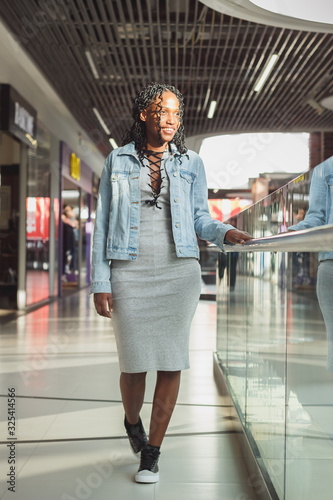 Young dark-skinned woman dressed in fashion clothes posing in the shopping center, blurred background