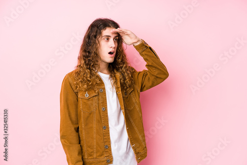 Young long hair man posing isolated looking far away keeping hand on forehead.