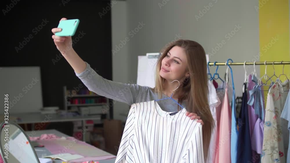 Attractive blond girl taking selfie with new dress on smartphone in tailor studio Attractive blond girl taking selfie with new dress on smartphone in tailor studio