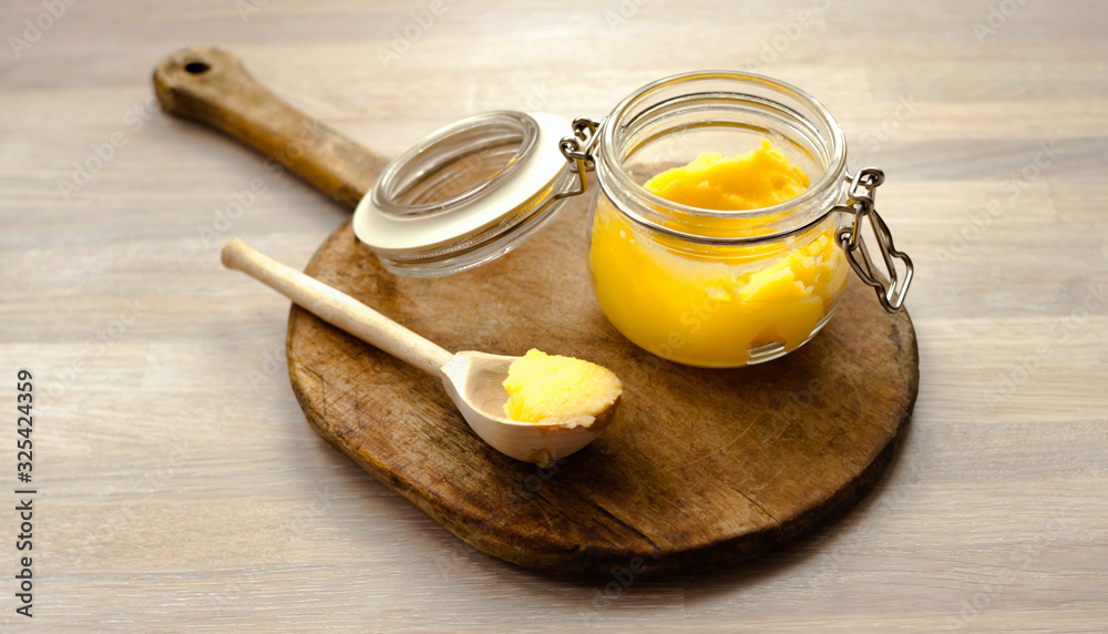 Ghee clarified butter desi in glass jar with spoon made from wood on natural wooden background Ghee clarified butter desi in glass jar with spoon made from wood on natural wooden background