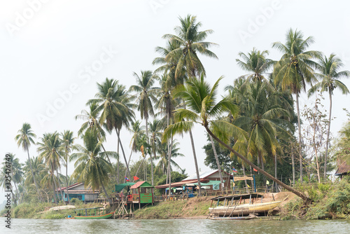 view of the shore with wooden houses and palm trees from a traditional boat in Don Khon island, Laos photo