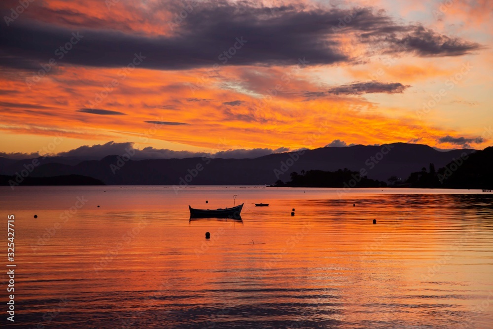 Boat moored at the bay, Sambaqui beach. Colorful orange and red clouds. Florianópolis, Santa Catarina / Brazil