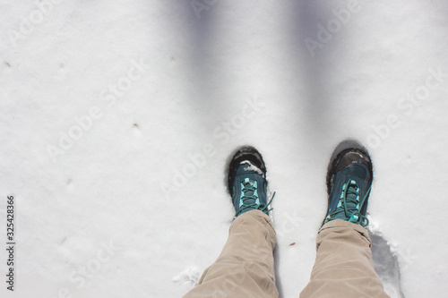 Top view of trekking shoes on the lava stone and snow background, female legs.