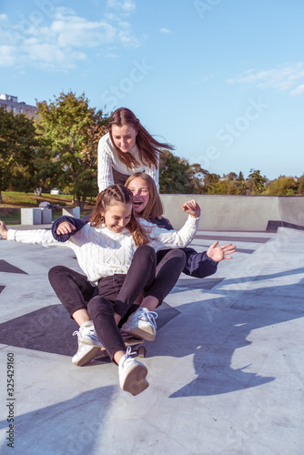 3 Young girls teenage schoolgirls ride skateboard summer park. Casual wear sweater jeans. Emotions happiness, fun, relaxation, smile laughter, best girlfriends, rest after college © byswat