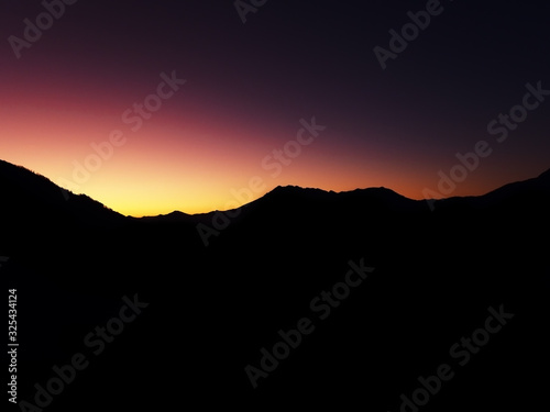 View of the dark outlines of a mountain range against the backdrop of an iridescent red-yellow sunset sky © jockermax3d