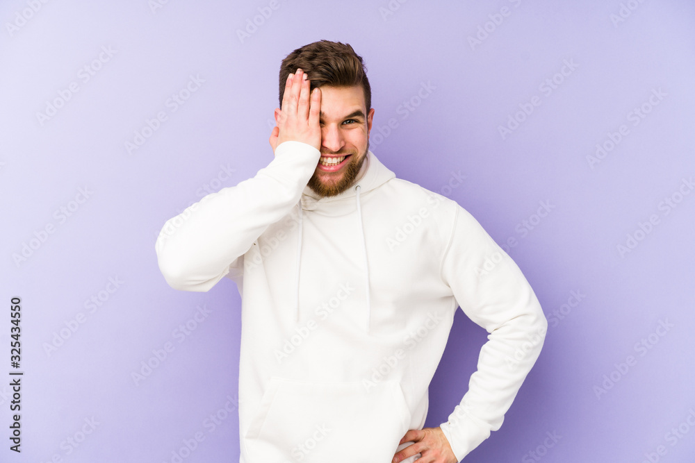 Young caucasian man isolated on purple background having fun covering half of face with palm. Young caucasian man isolated on purple background having fun covering half of face with palm.
