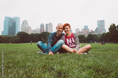 Happy couple enjoying romantic vacation outdoors in Central Park, New York City, USA. Smiling tourists man and woman in summer sun sitting on grass in Manhattan. Dating young couple happy in love.