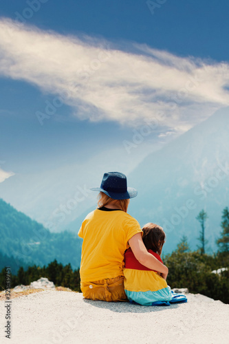 Backs of a mother and daughter hugging while looking down from the top of mountain into the sunny and misty valley