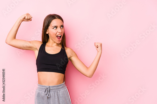 Young caucasian fitness woman posing in a pink background raising fist after a victory, winner concept.