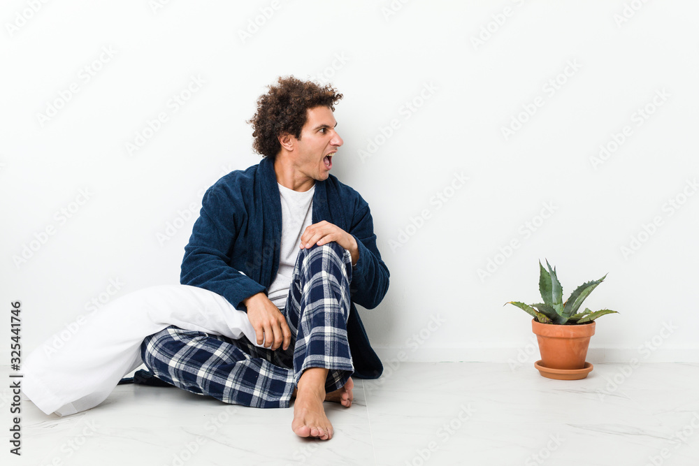Mature man wearing pajama sitting on house floor shouting towards a copy space