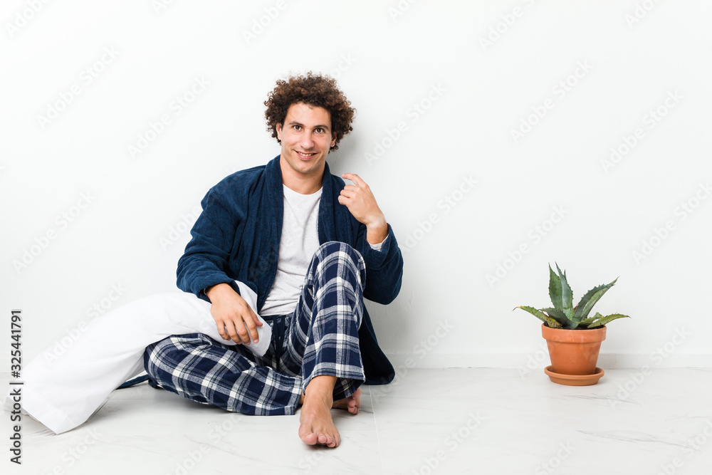 Mature man wearing pajama sitting on house floor pointing with finger at you as if inviting come closer. Mature man wearing pajama sitting on house floor pointing with finger at you as if inviting come closer.
