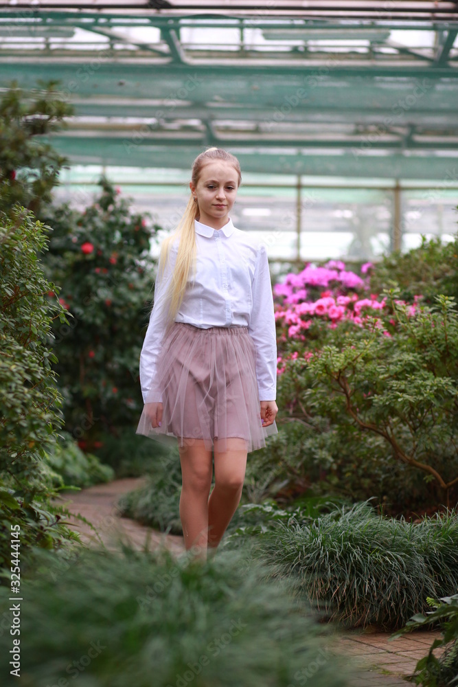 Young girl with long white hair in a white formal shirt and a short light skirt walks in the garden with blooming azalea Young girl with long white hair in a white formal shirt and a short light skirt walks in the garden with blooming azalea