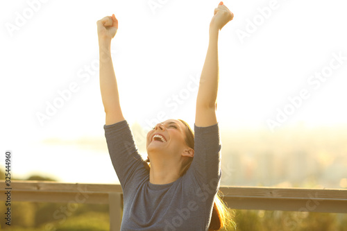 Excited woman raising arms at sunset in a park