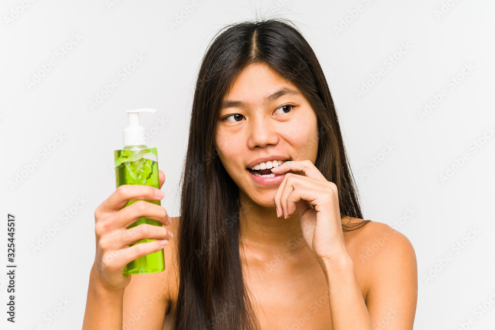 Young chinese woman holding a moisturizer with aloe vera isolated relaxed thinking about something looking at a copy space. Young chinese woman holding a moisturizer with aloe vera isolated relaxed thinking about something looking at a copy space.