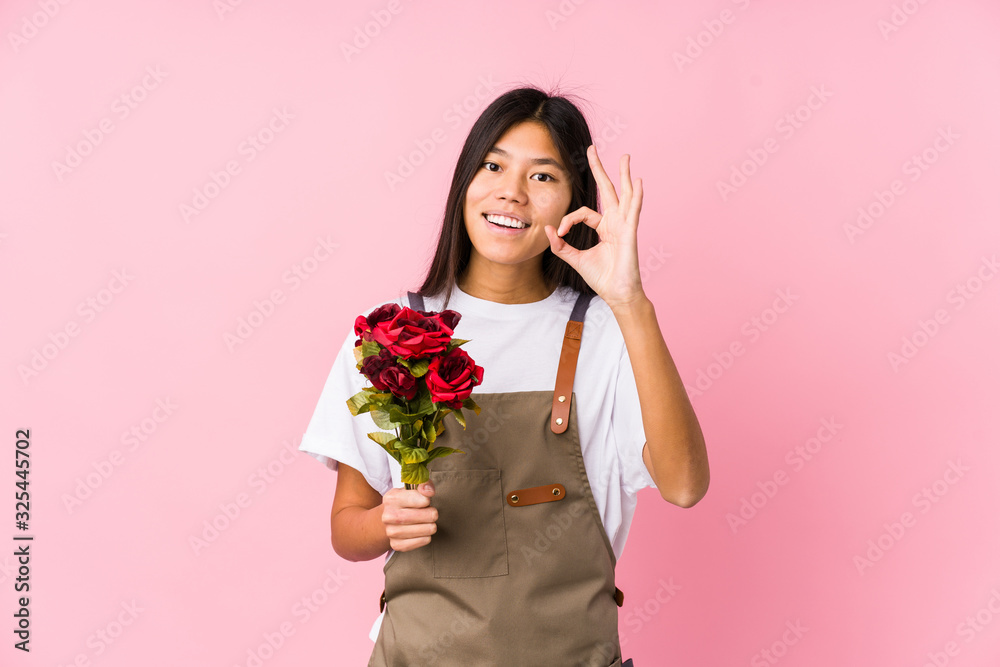 Young chinese gardener woman holding a roses isolated cheerful and confident showing ok gesture. Young chinese gardener woman holding a roses isolated cheerful and confident showing ok gesture.