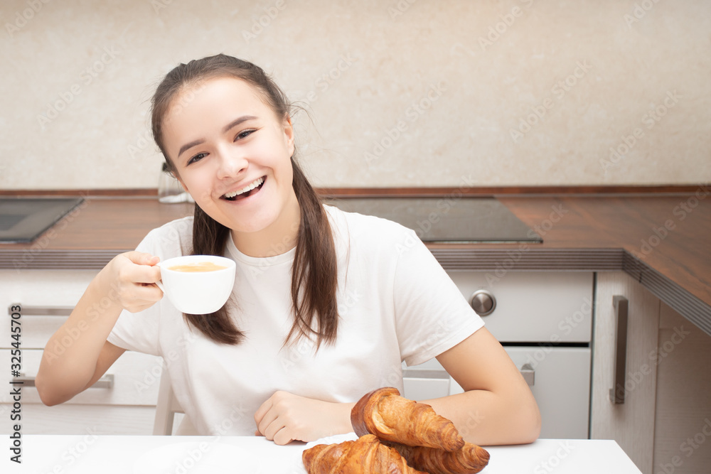 European girl in the morning at home having breakfast with croissants, drinking coffee, smiling. European girl in the morning at home having breakfast with croissants, drinking coffee, smiling.