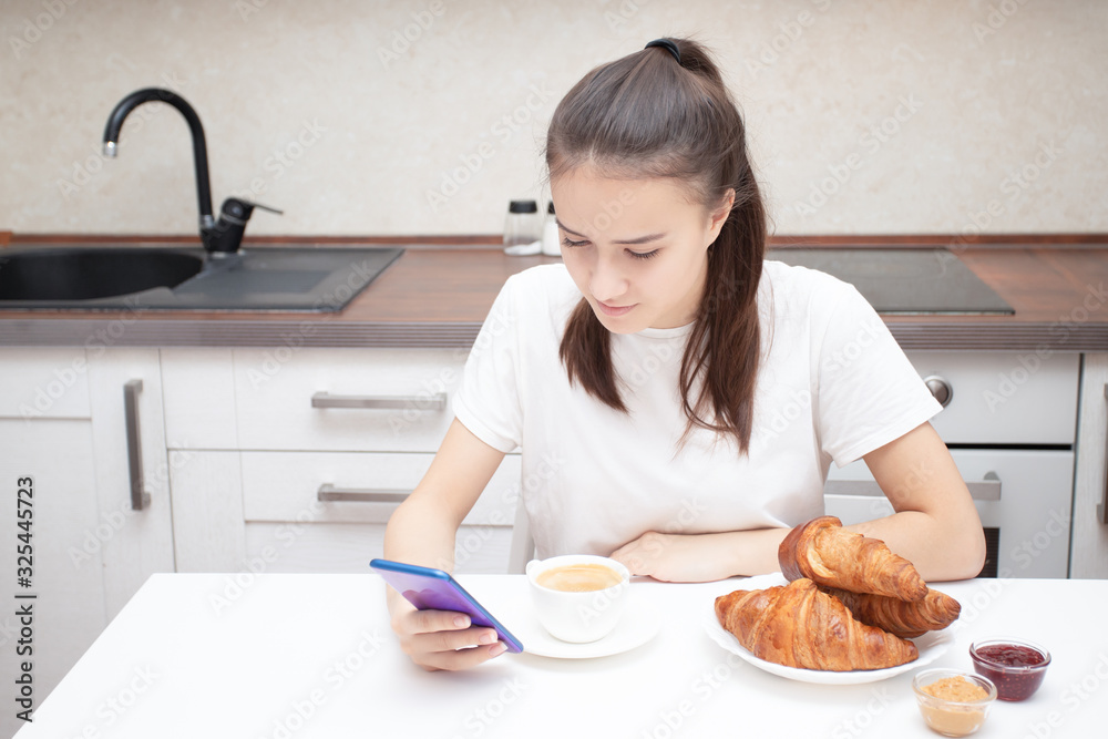 Young European girl reads the news on a smartphone in the morning at breakfast