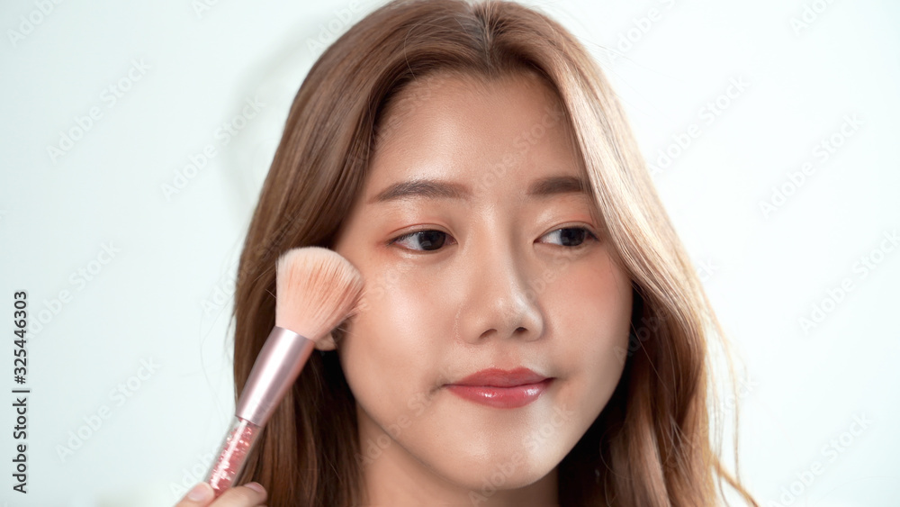 Beautiful woman makes blush on the face using makeup brush sitting in the bedroom. Asian woman makes makeup oneself. Beautiful woman makes blush on the face using makeup brush sitting in the bedroom. Asian woman makes makeup oneself.