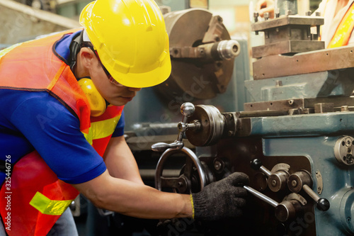 A mechanical engineer or worker with yellow safety helmet and goggles at work on production in a factory.