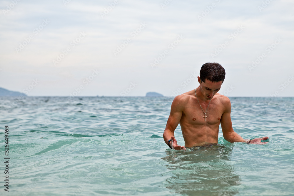 Young handsome man posing in water near ocean.