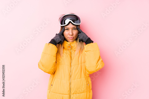 Young caucasian woman wearing a ski clothes in a pink background focused on a task, keeping forefingers pointing head.