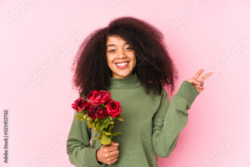 Young afro woman holding a roses isolated Young afro woman holding a rosesjoyful and carefree showing a peace symbol with fingers.