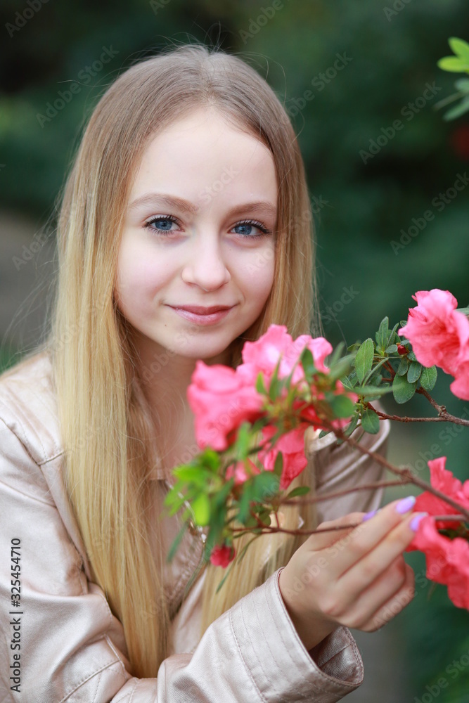 Young girl with long blond hair in a powdery jacket  enjoys in the garden with blooming azalea