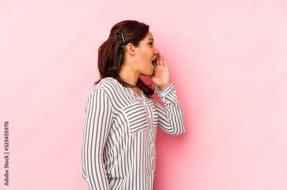 Middle age latin woman isolated on a pink background shouting and holding palm near opened mouth. Middle age latin woman isolated on a pink background shouting and holding palm near opened mouth.