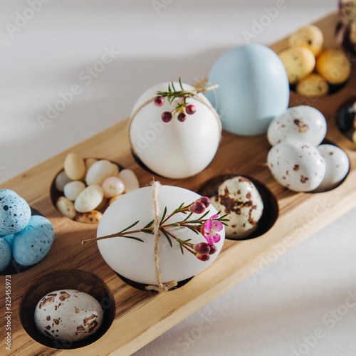 Natural Colored Eggs with flowers, easter chocolate eggs, candy and jelly bean in wooden egg box with sunlights. Stylish Compositions.
