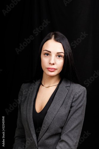 Portrait of young business woman in a grey jacket on black background