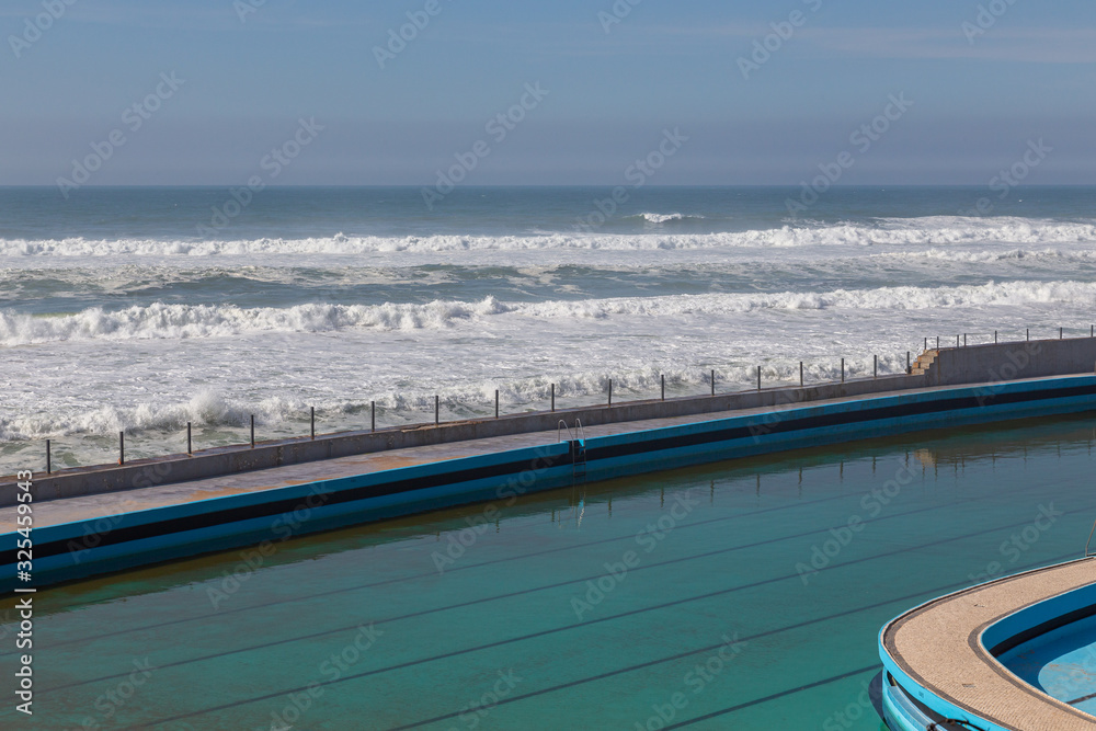 Swimming pool on ocean coast, moviment waves with foam. Wind power. Turquoise water.