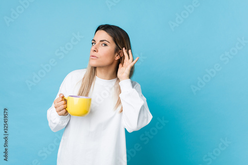 Young caucasian woman holding a coffee cup trying to listening a gossip.