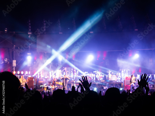 crowd at concert - summer music festival in front of bright stage lights. Dark background, smoke, concert spotlights.people dancing and having fun in summer festival party outdoor