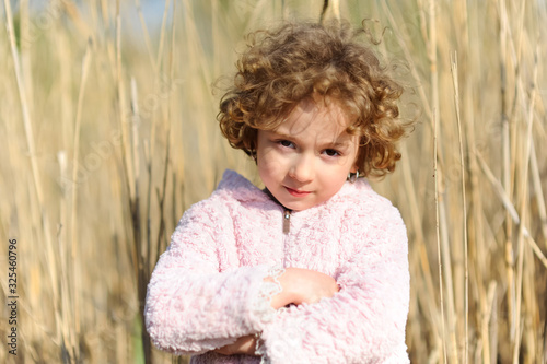 Cute, beautiful curly little girl close-up portrait outdoors. Serious toddler child, kid on a sunny day on the nature field at summer or spring.