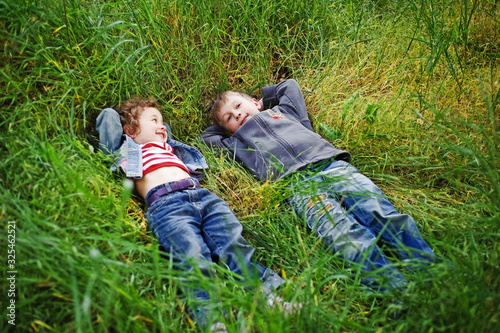 Boy and girl are resting on the green grass in summer. Happy children, kids, brother and sister, friends lying on grass on picnic on the nature. Funny kids relax, play outdoors in park. Top view.