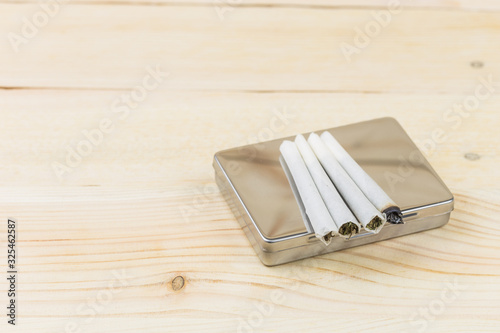 Joint of cannabis on cigarette box for smoking, on wooden background.