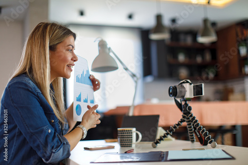 Young business woman recording video for her vlog shows papers with graphs photo