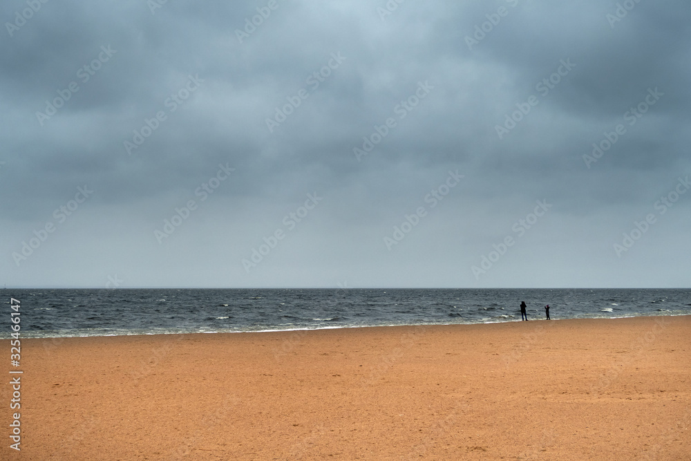 Stormy winter beach scene with two silhouette people