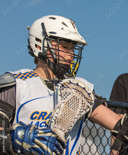 Close up of teen at a lacrosse game with his helmet and face mask on and a clear blue sky